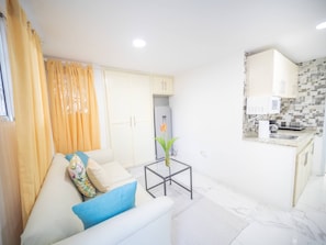 A modern living room with a sofa, a glass coffee table, and a kitchen area with cabinets and a tiled backsplash. - Studio In Sosua Center! Strip Zone (Sosúa)