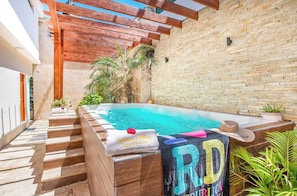 A swimming pool with a wooden deck, a stone wall, and a pergola overhead. - Spacious 1BR APT in Sosua Strip! (Sosúa)