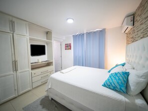 A bedroom with a bed, a television, a wardrobe, and a bathroom door. - Cozy & Central 3BR Apt Secure & Comfortable (Sosúa)