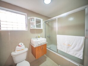 A bathroom with a toilet, a sink, a glass shower enclosure, and a window with blinds. - Cozy & Central 3BR Apt Secure & Comfortable (Sosúa)