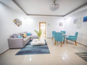 Ein modernes Wohnzimmer mit einer Eckcouch, einem Couchtisch, einem Essbereich mit Tisch und Stühlen sowie einem Deckenventilator.