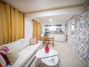 Una sala de estar con sofá, una mesa de comedor y una cocina al fondo.