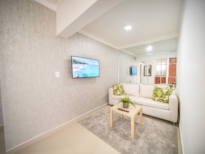 A modern living room with a flat-screen TV, a sofa, a coffee table, and a mirror reflecting the room. - 2BR APT in Sosua Center Strip Zone (Sosúa)