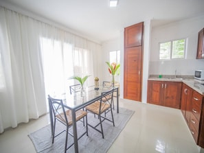 A modern kitchen with wooden cabinets, a glass dining table, and a view of the outdoors. - 2BR APT in Sosua Center Strip Zone (Sosúa)