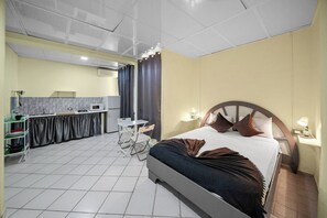 A hotel room with a bed, bedside lamps, a small desk, a chair, a kitchen area with a microwave, and a curtain. - Cheap Hotel Room in Sosua Strip! (Sosúa)
