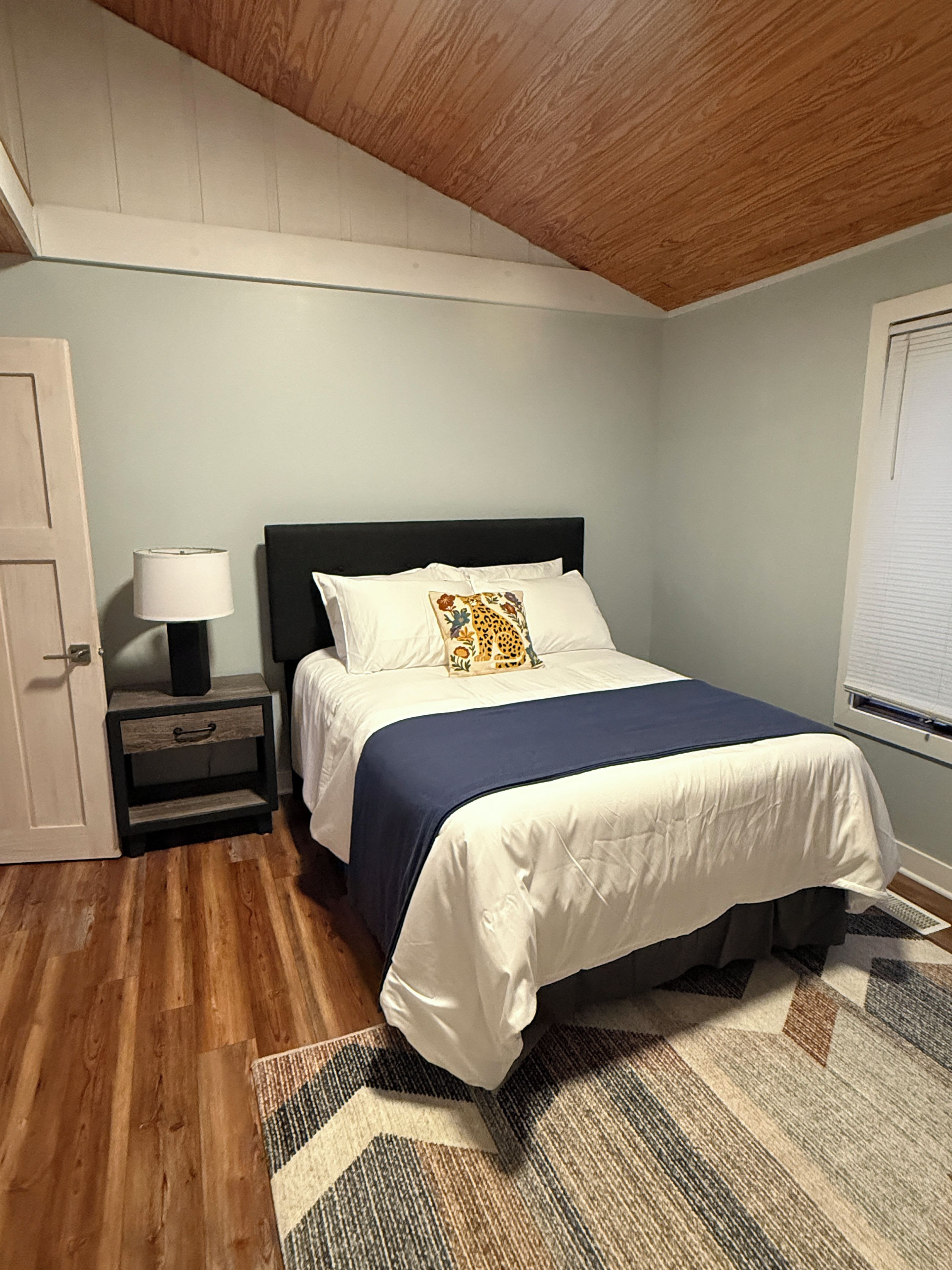 A bedroom with a bed, nightstand, lamp, and a window with blinds.