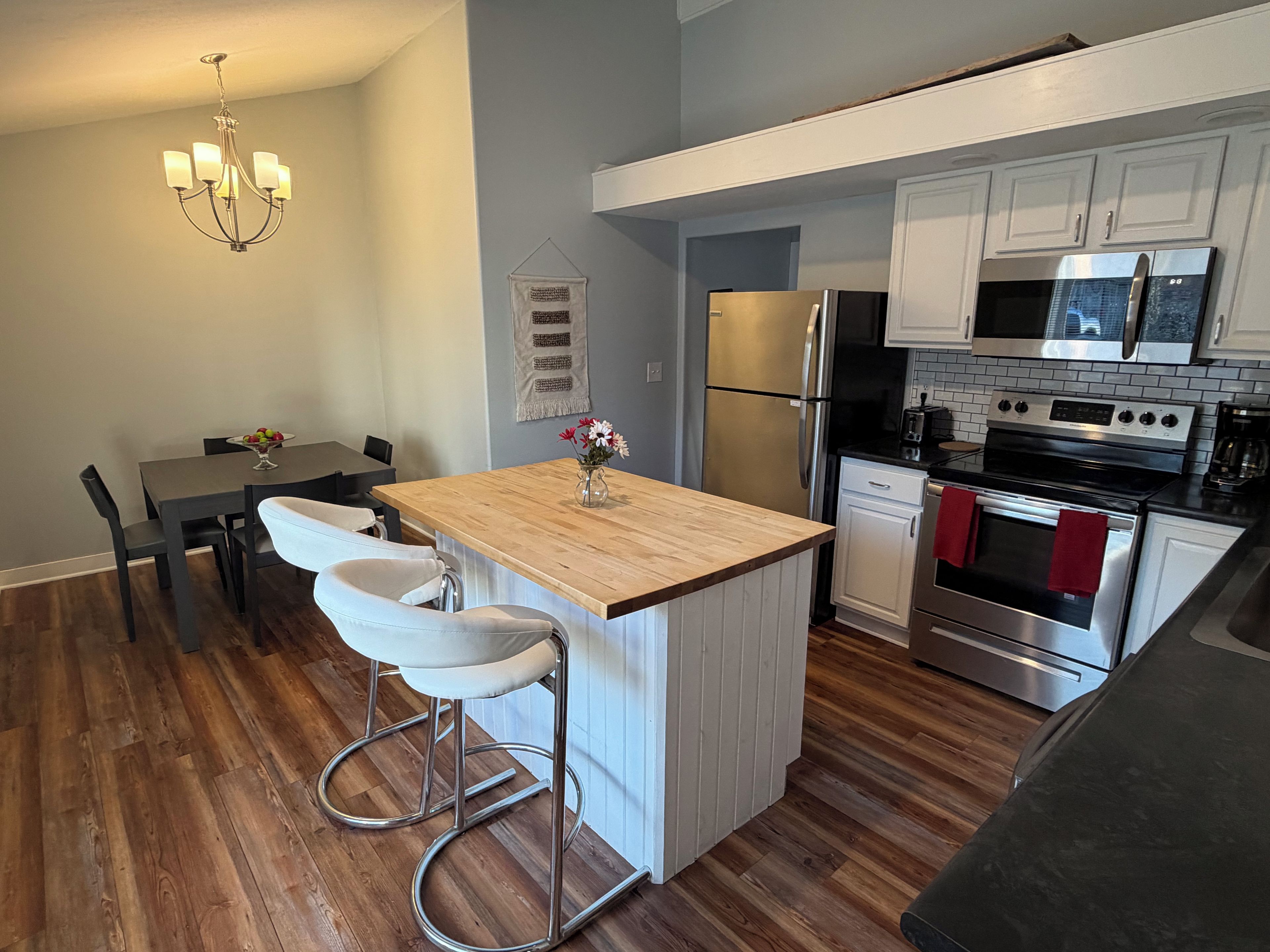 A modern kitchen with a wooden island, stainless steel appliances, and a dining area with a chandelier.