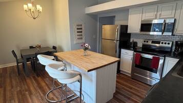 A modern kitchen with a wooden island, stainless steel appliances, and a dining area with a chandelier.