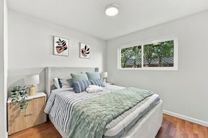 A bedroom with a bed, bedside tables, a window with a view, and two wall-mounted artworks. - Single-Story 4BR · King Suite · Treehouse & Deck (Pleasanton)