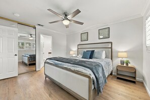 Une chambre à coucher comprenant un lit, une table de chevet, un ventilateur de plafond et une porte donnant sur une autre pièce.
