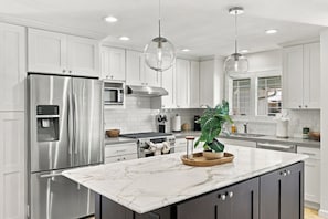 A modern kitchen with white cabinetry, stainless steel appliances, a marble countertop, and pendant lighting. - Single-Story 4BR · King Suite · Treehouse & Deck (Pleasanton)