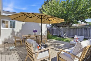 Une terrasse en bois avec des meubles d’extérieur, notamment des chaises et une table, placée sous un grand parasol.