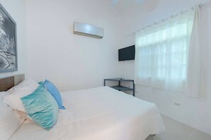A bedroom with a bed, a flat-screen TV mounted on the wall, a bedside table, and a window with curtains. - Hispaniola Villa No26 Near Sosua Beach (Sosúa)