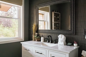 A bathroom with a white vanity, a black-framed mirror, and a window with a view of trees. - Lookout MTN Escape - Hot Tub - Fire Pit - Arcade (Golden)