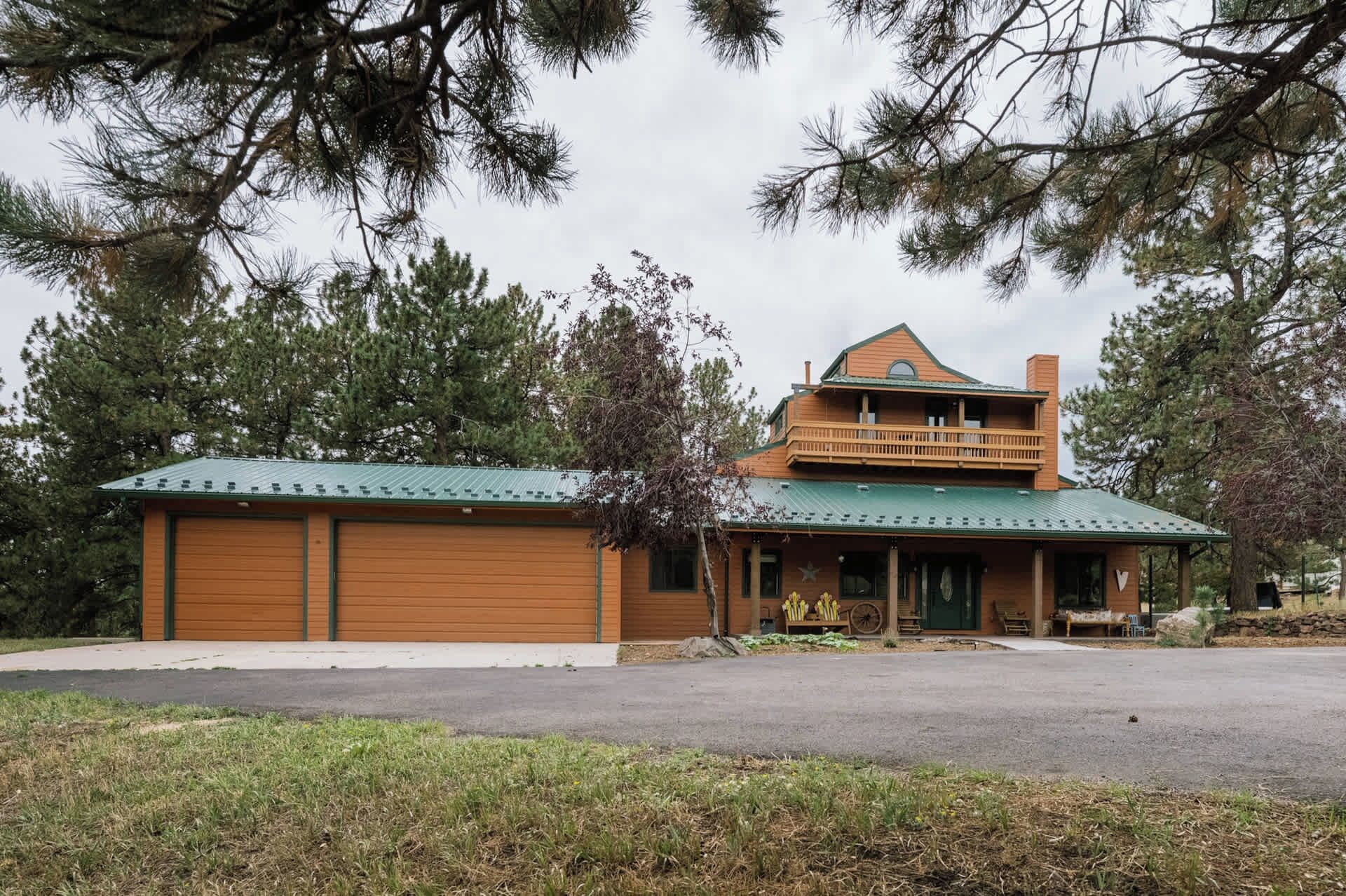 A two-story wooden cabin with a green roof, a balcony on the upper floor, and a front porch with a bench.