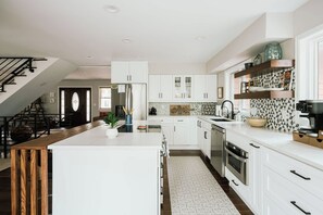 A modern kitchen with white cabinetry, a central island, and a staircase leading to a loft area. - Lookout MTN Escape - Hot Tub - Fire Pit - Arcade (Golden)
