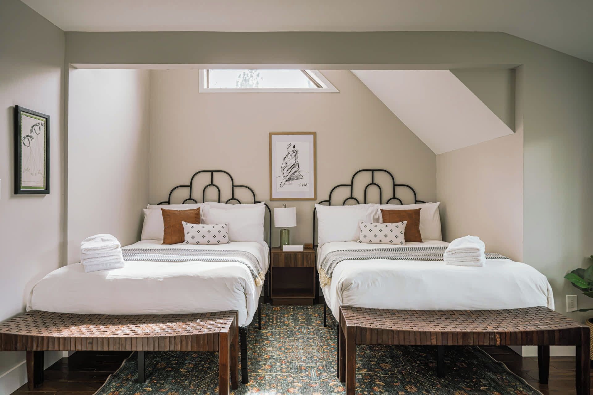 A hotel room with two beds, a skylight, a patterned carpet, and a framed artwork on the wall.