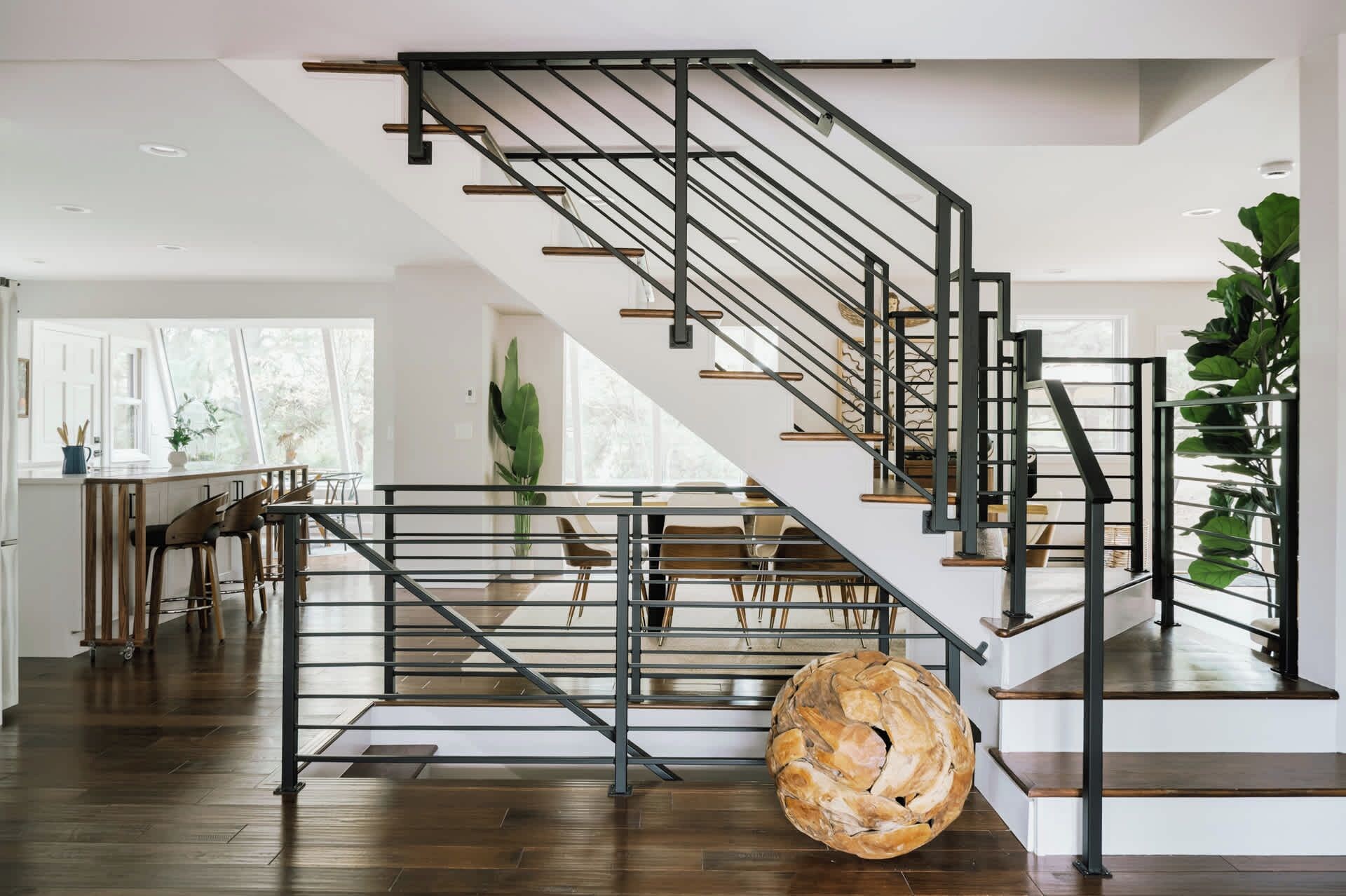 Eine moderne Treppe mit Metallgeländer und Holzstufen, die zu einem Essbereich mit Stühlen und einem Tisch führt.