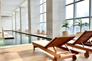 Uma área moderna de piscina interna com espreguiçadeiras e plantas em vasos.