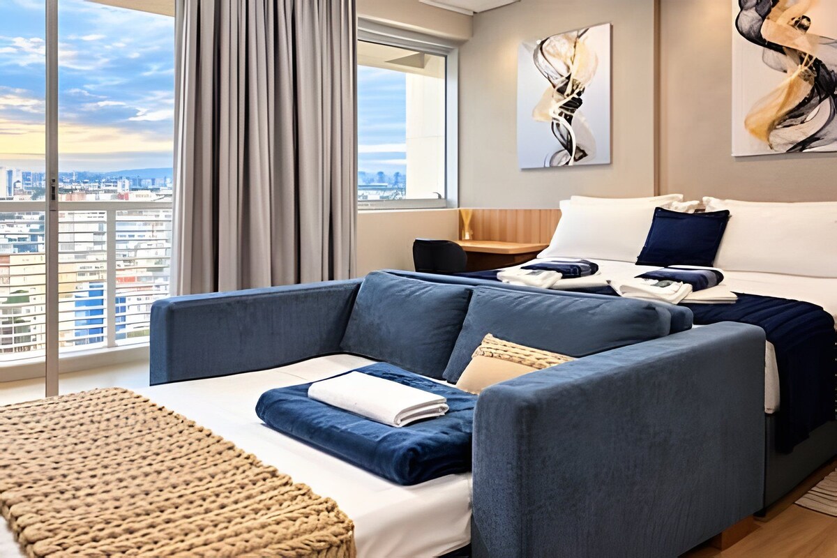 A modern hotel room with a large window, a sofa, a bed, and abstract wall art.
