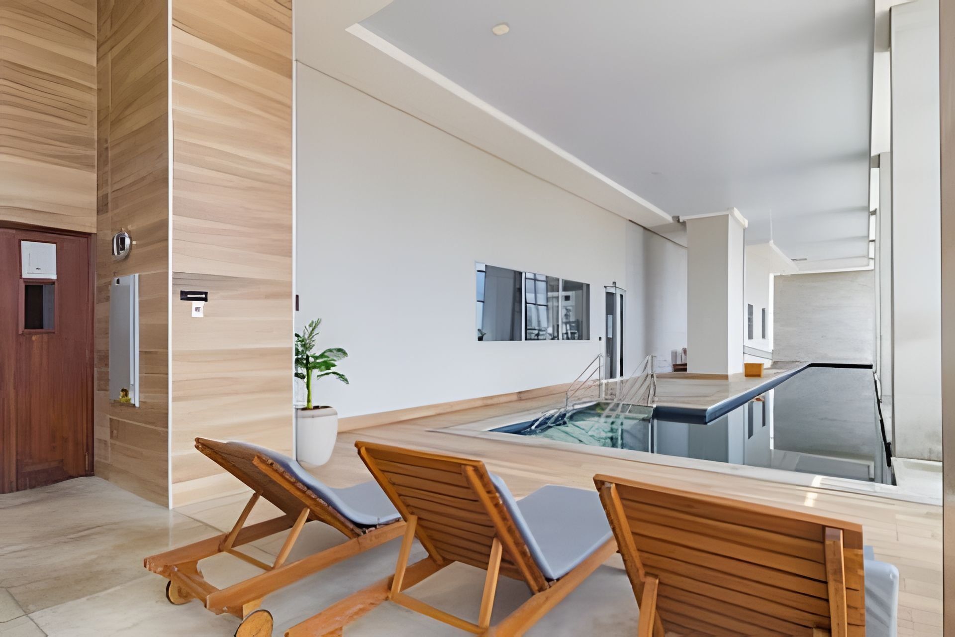 Un interior moderno con zona de piscina, sillones de madera y una planta en maceta.