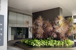 A modern indoor space with a reception area, a glass wall, and a planter with various plants. - Prime Studios Centro Osasco15min Alpha (Osasco)
