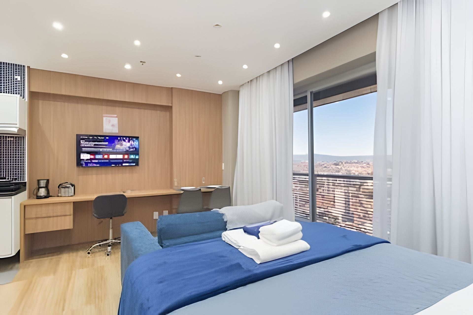 A hotel room with a bed, a desk, a chair, a television, and a large window with a view.