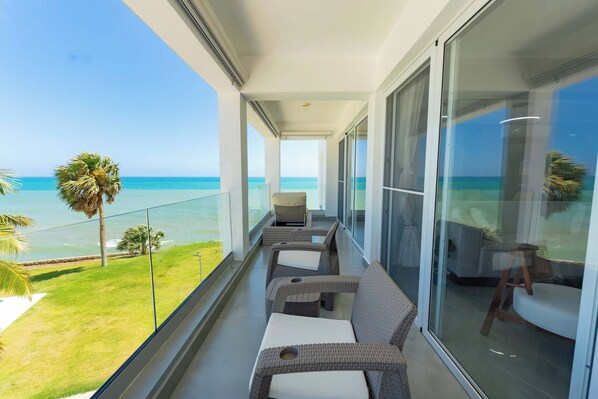 A balcony with wicker furniture, a glass door, and a view of the ocean.
