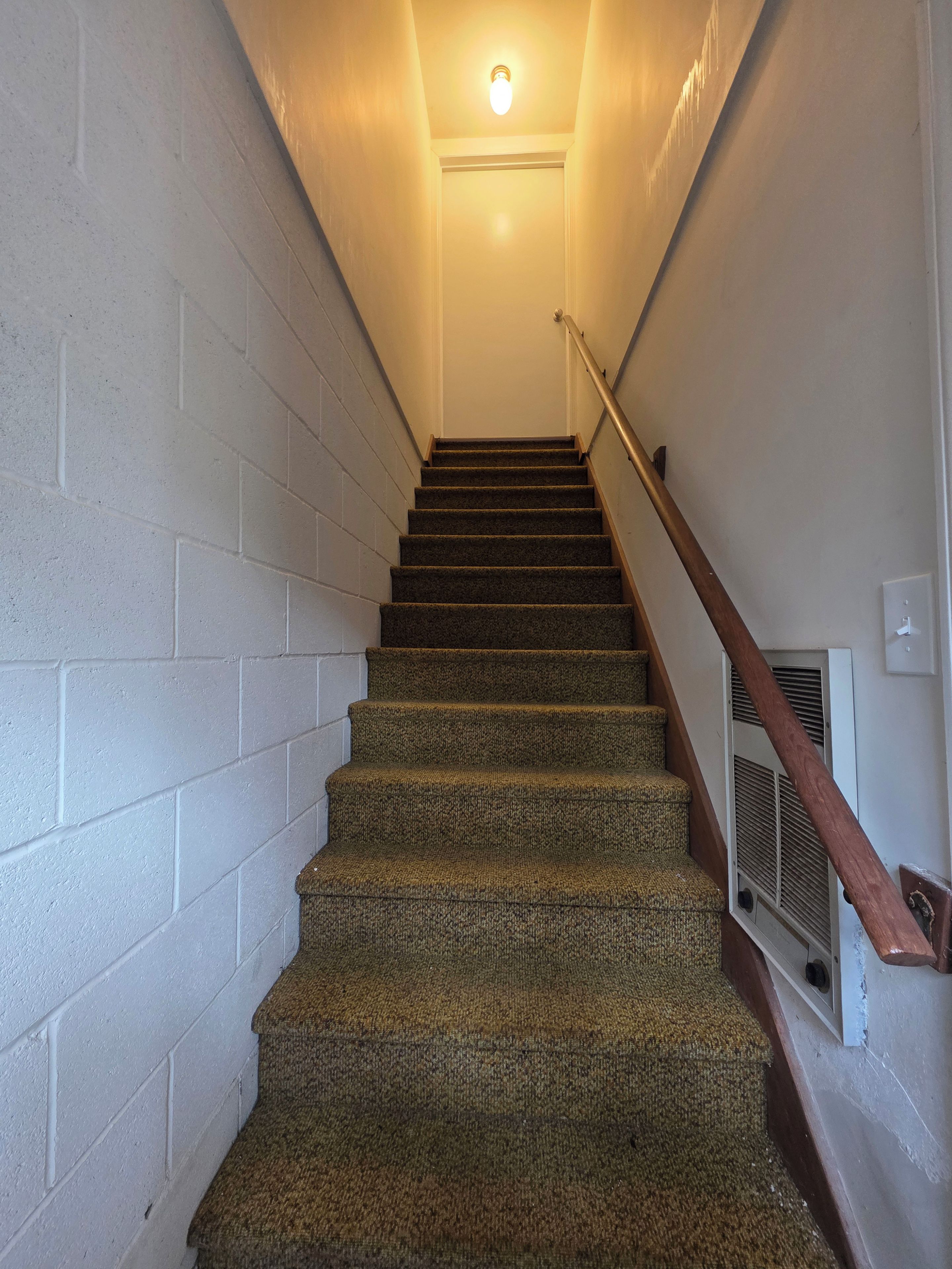 Una escalera con peldaños alfombrados, paredes blancas y barandilla de madera.