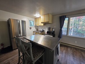 Cozinha moderna com eletrodomésticos de aço inoxidável, uma ilha central e janela com vista para árvores.