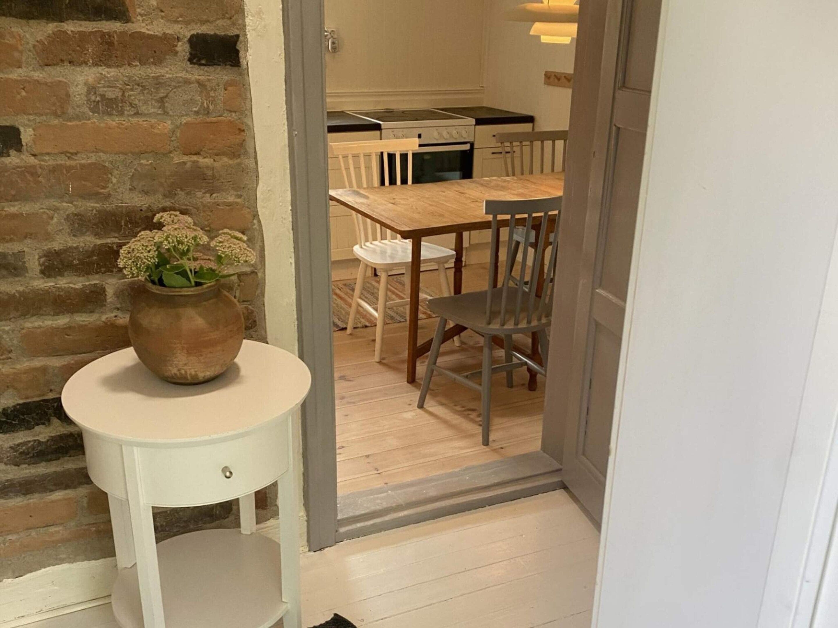 Una habitación con una mesa blanca, una silla de madera y una planta en maceta.