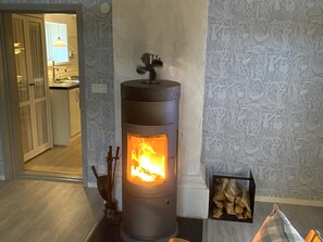 A room with a wood-burning stove, a door leading to a kitchen, and patterned wallpaper. - 4 Person Holiday Home in Garphyttan (Garphyttan)