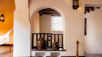 A hallway with a bench, two vases, a candle, and a window with barred glass.