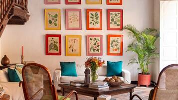 A cozy living room with a wooden staircase, a ceiling fan, and a wall adorned with framed botanical prints.