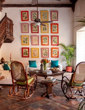 A cozy living room with a wooden staircase, a ceiling fan, and a wall adorned with framed botanical prints. - Gorgeous house for rent in Cartagena, Colombia (Cartagena de Indias)