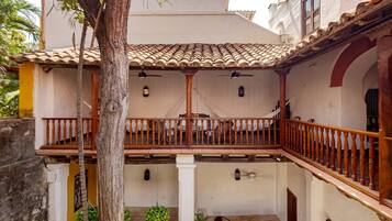 Um pátio com telhado de azulejos, grades de varanda de madeira e uma mesa com cadeiras.