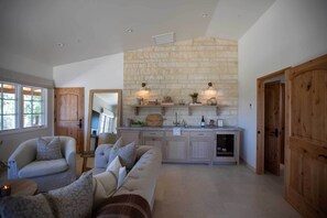 A spacious living area with a stone wall, wooden cabinets, and a built-in kitchen. - Sunstone Cottage the Bordeaux Suite (Santa Barbara County)