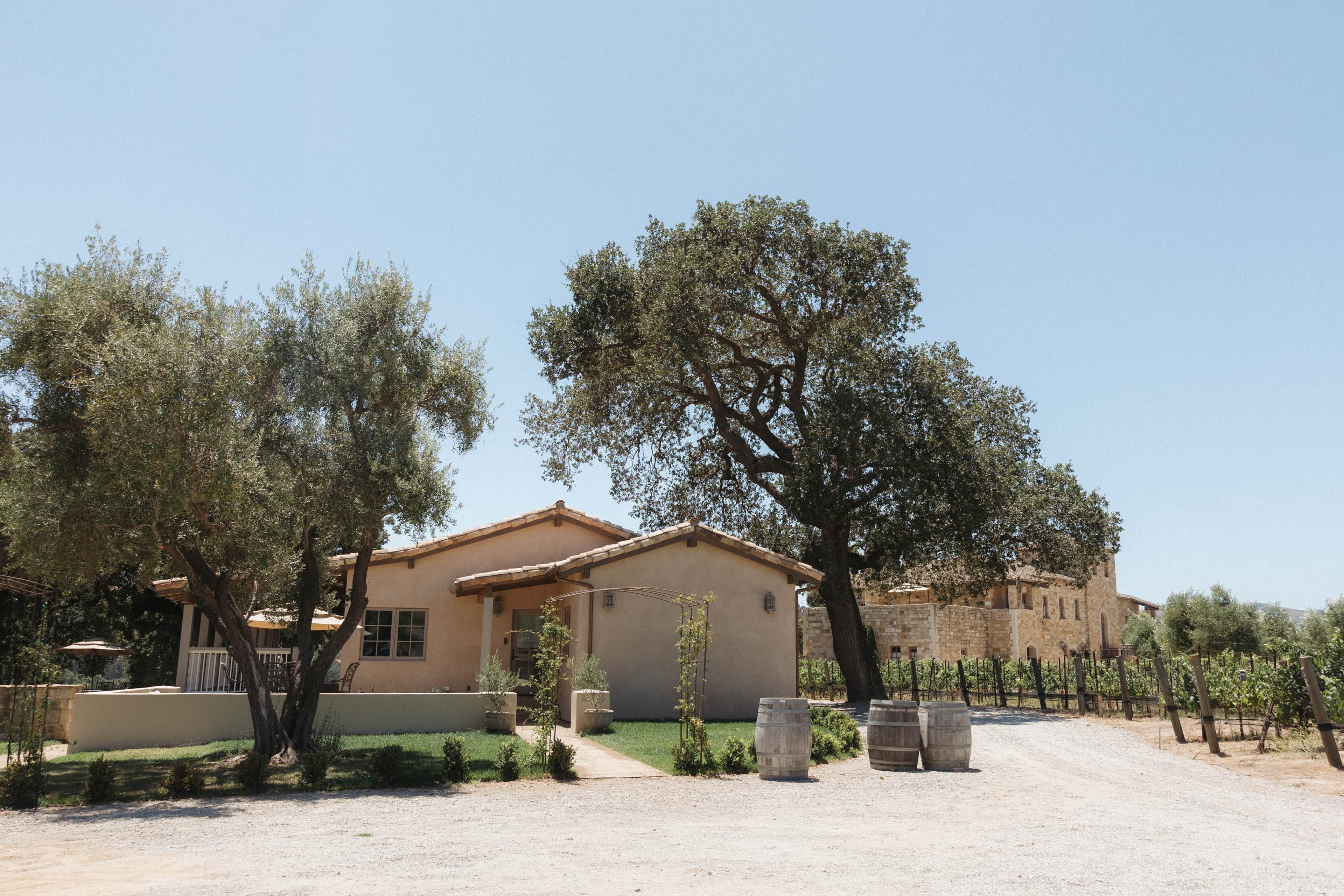 A building with a tiled roof, surrounded by trees and a gravel driveway.