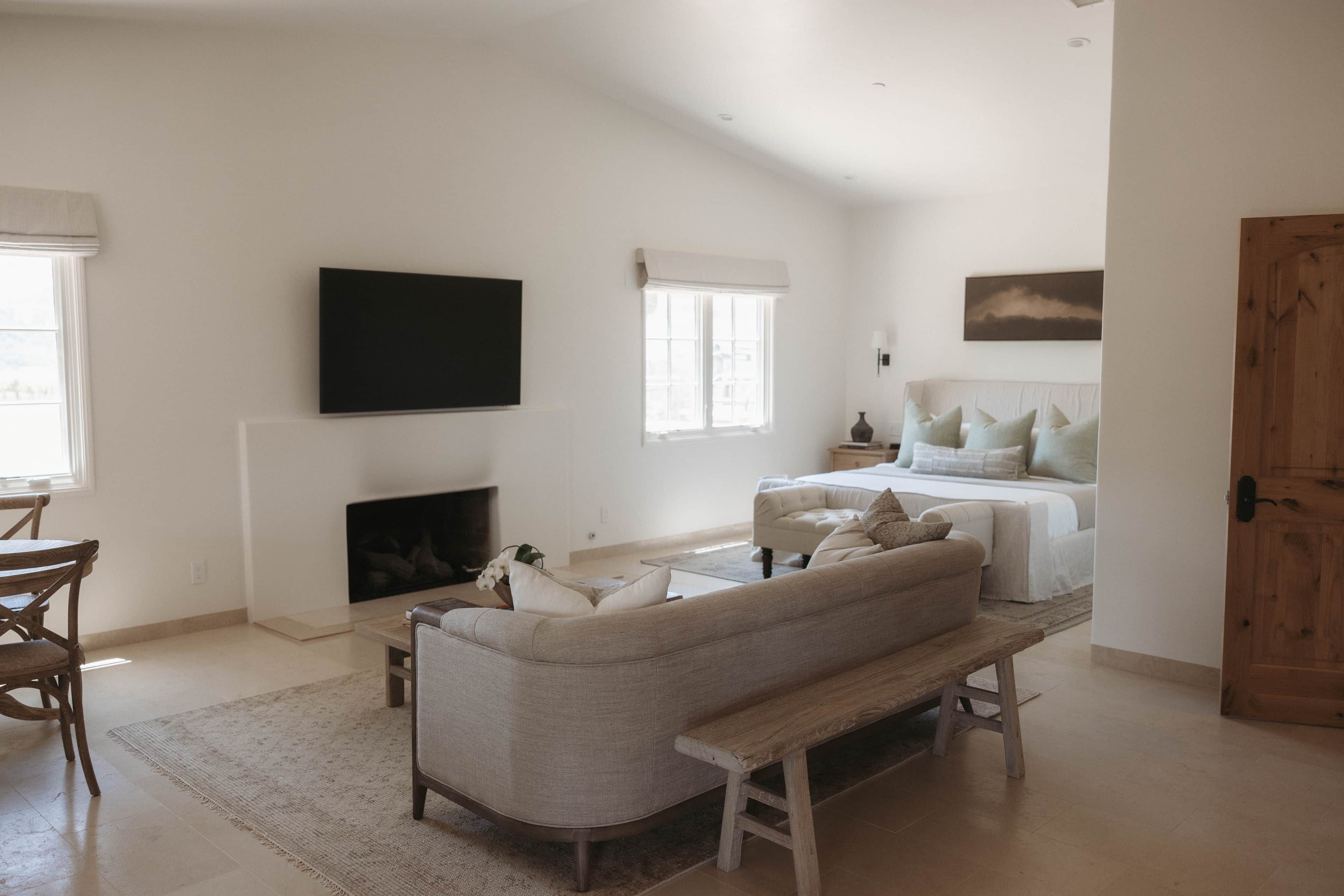 A living room with a sofa, a bench, a fireplace, a television mounted on the wall, and a door.