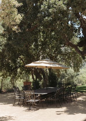 An outdoor dining area with a table and chairs under a large tree. - Sunstone Cottage the Champagne Suite (Santa Barbara County)
