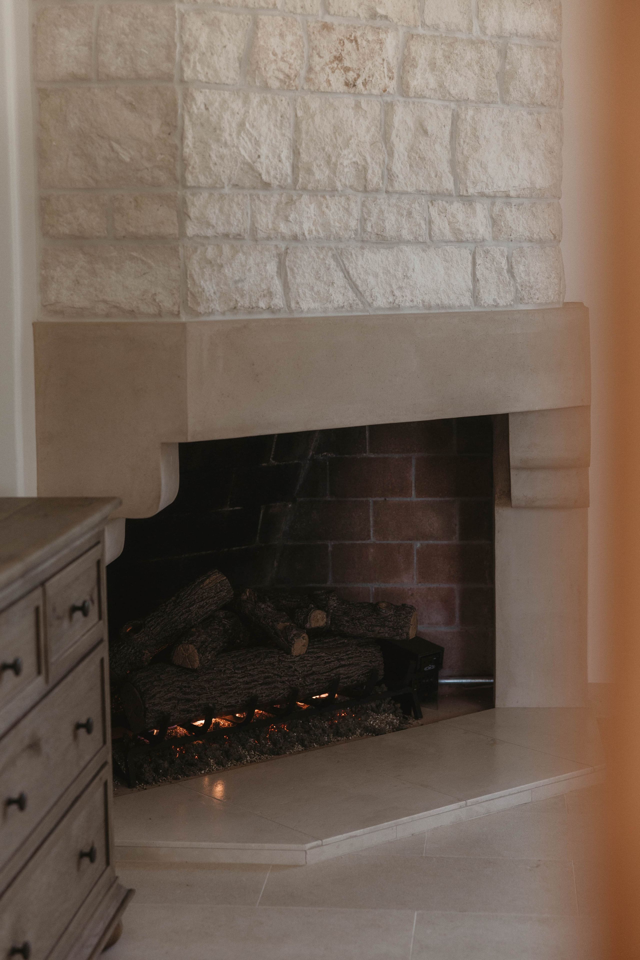 A fireplace with a stone mantle and a brick interior, surrounded by a tiled floor.
