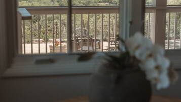 Uitzicht vanuit een raam met balkon, met zicht op een landschap met heuvels en bomen.
