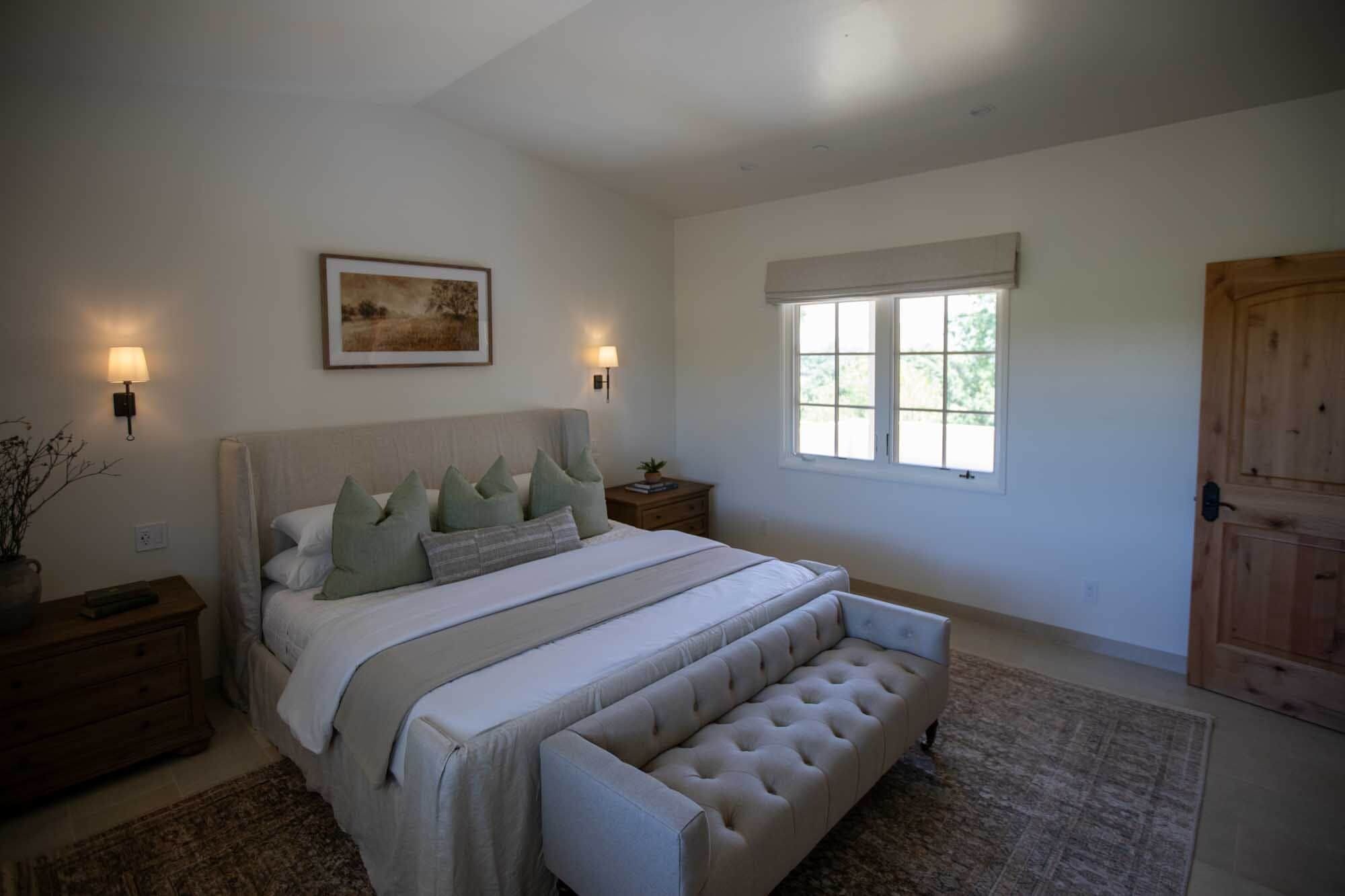 A bedroom with a bed, bedside lamps, a window, and a door.
