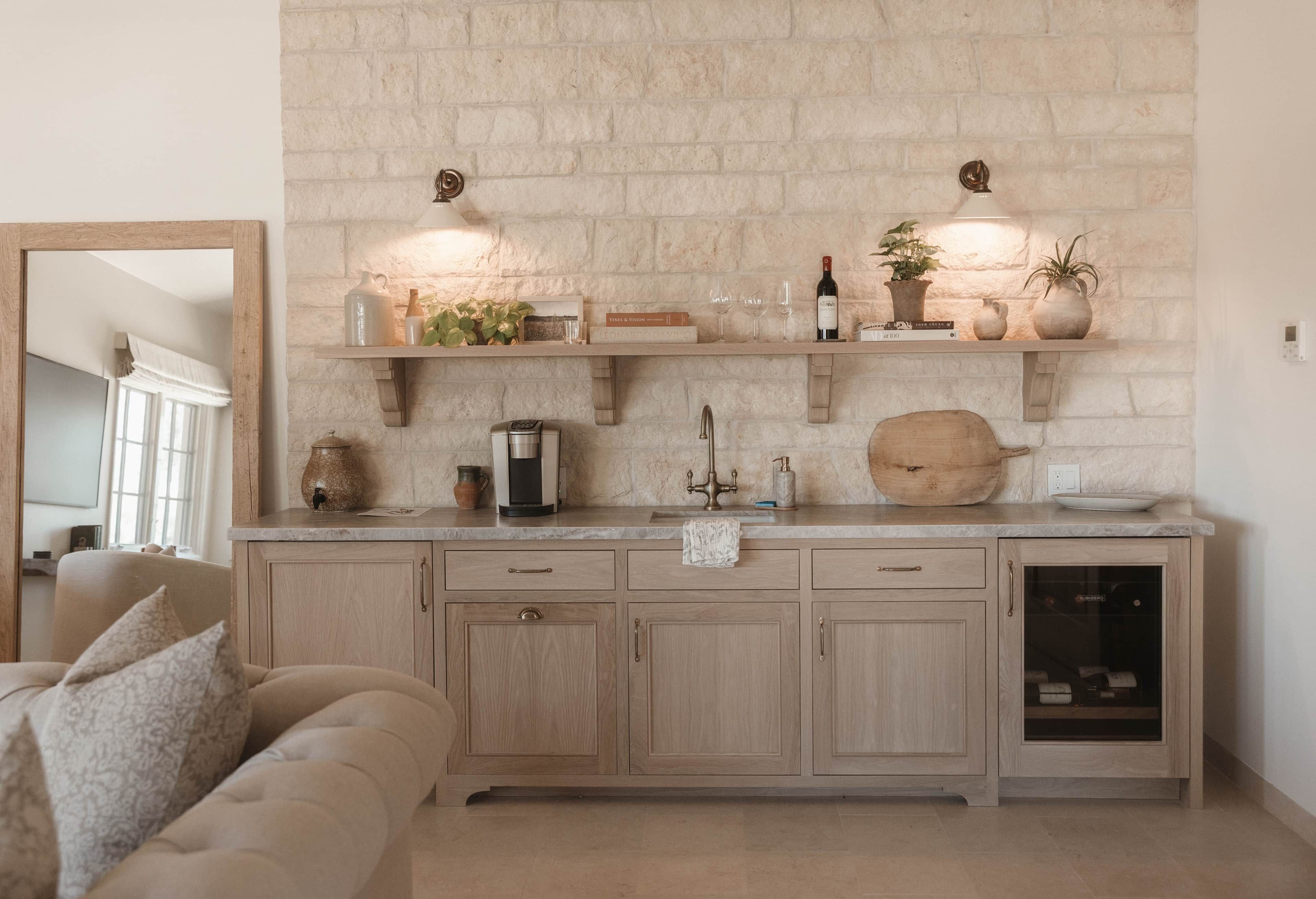 A kitchen with a stone wall, wooden cabinets, a coffee machine, and a wine bottle on the countertop.