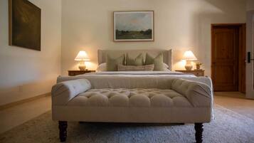 A bedroom with a large bed, two bedside lamps, a painting on the wall, and a door to the right.