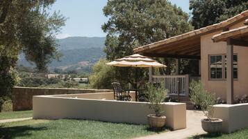 An outdoor patio area with a table and chairs, a pergola with an umbrella, and a view of the surrounding landscape.