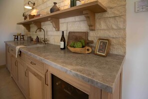 Una cocina con pared de piedra, armarios de madera, una botella de vino y un marco de fotos.