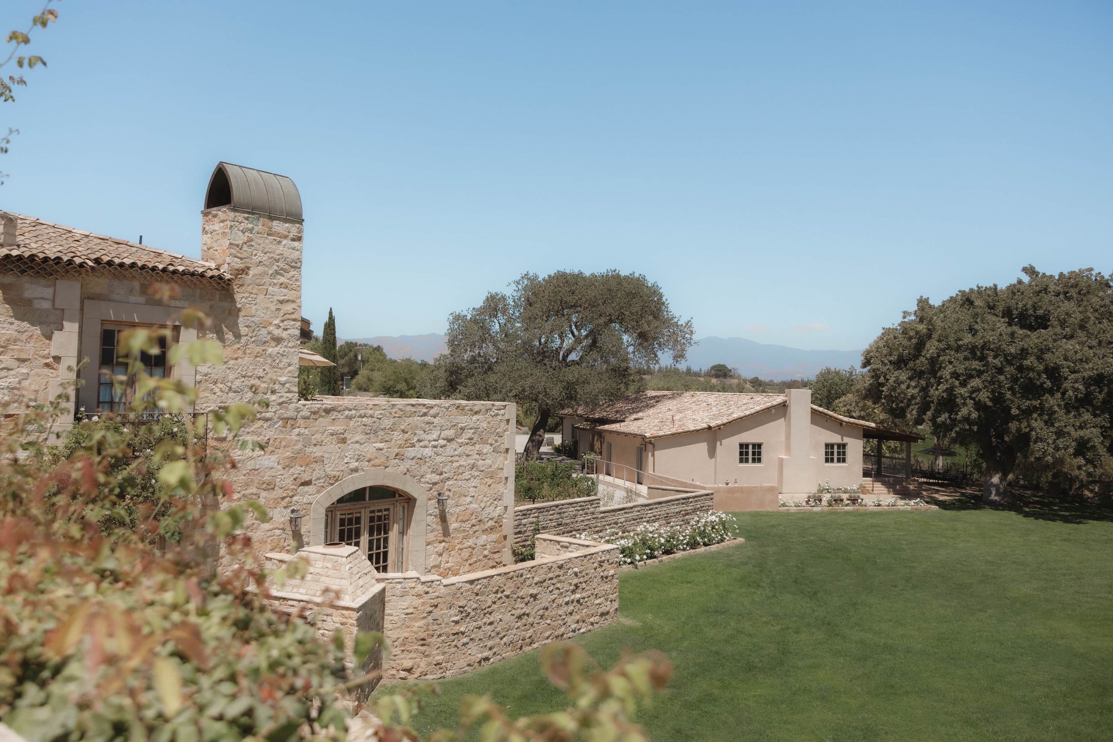 A stone building with a tiled roof, a stone wall, and a grassy lawn.