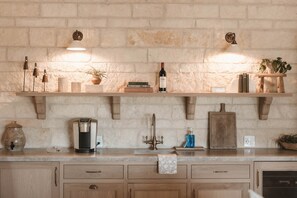 A kitchen with wooden shelves, a coffee maker, a wine bottle, and a plant.