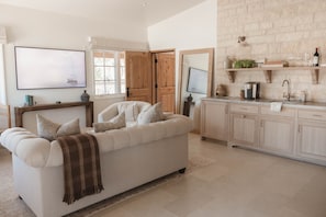 A living room with a sofa, a coffee machine, and a kitchen area with cabinets and a countertop.